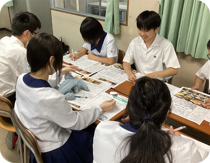 4人の学生が真剣な表情で、机の上に広げられた書類に書き込みながら話し合っている