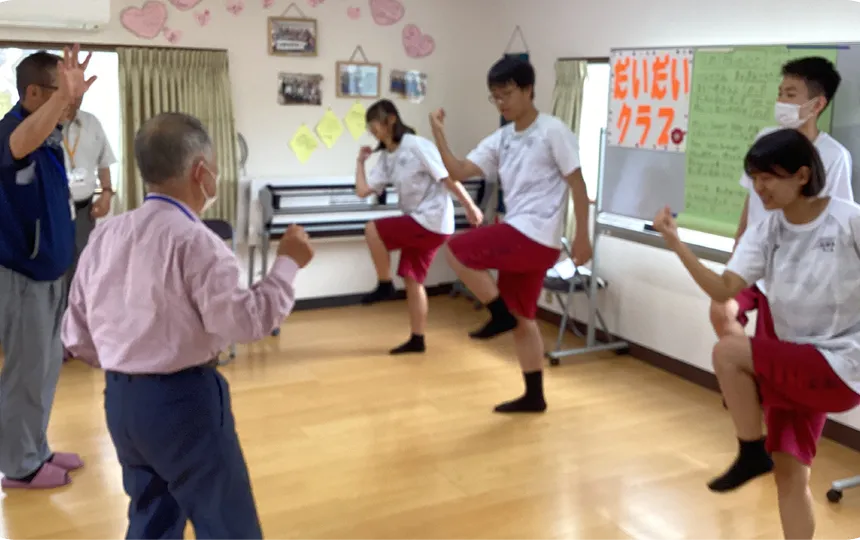 広い室内で、体操をしている学生と高齢者たち