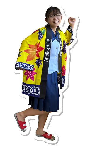 女子学生が夏の制服の上にハッピを着て、笑みを浮かべ、右腕を軽く上げ、左足も少し上げて楽しそうにポーズをとっている