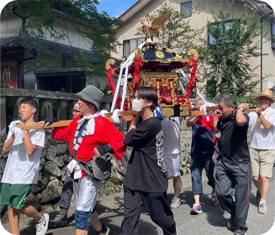 複数の学生と大人の男性たちが、協力して神輿を担いでいる