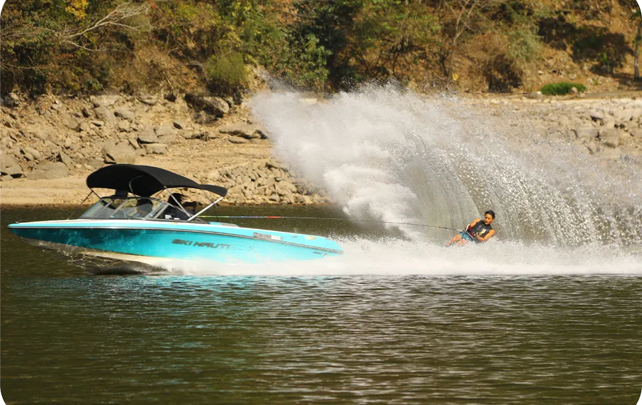 青いモーターボートに引っ張られ、水上スキーをしている人が写っている人がおり、水面には大きな水しぶきが上がっている。
